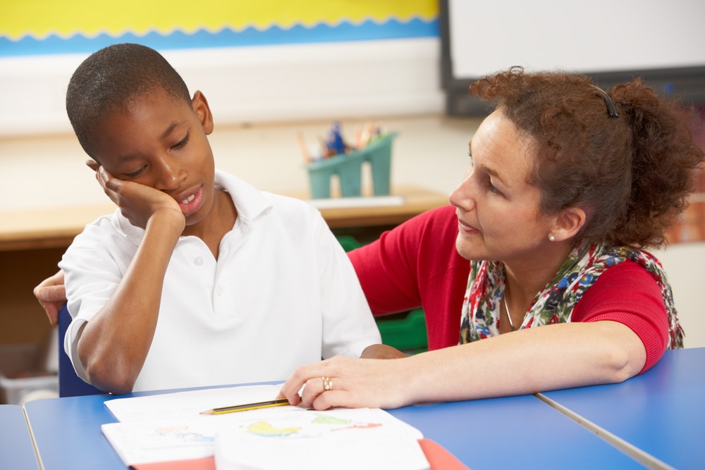 signs of anxiety in children- teacher talking to upset boy in class